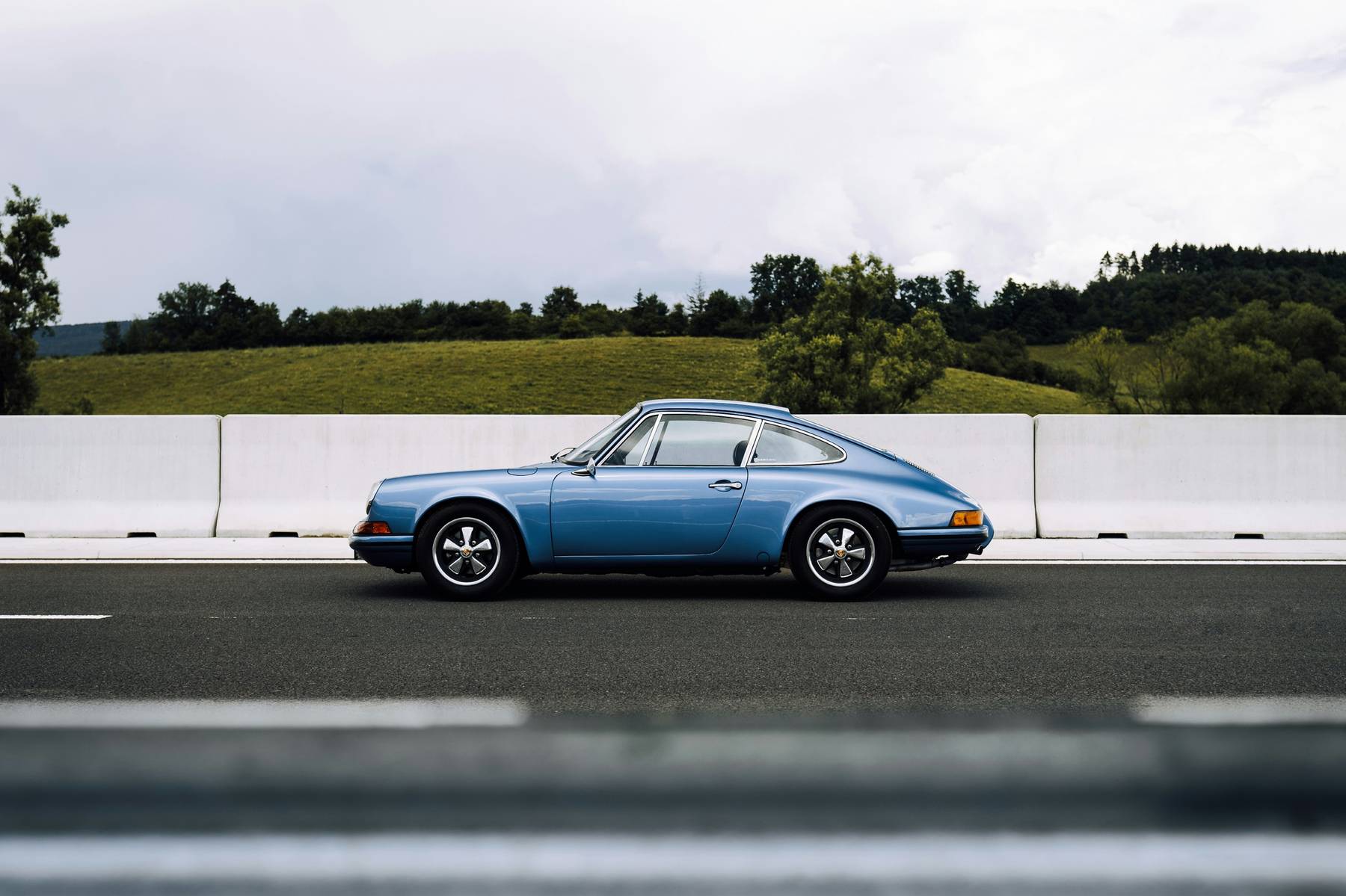 Porsche 911 clásico azul de perfil en carretera