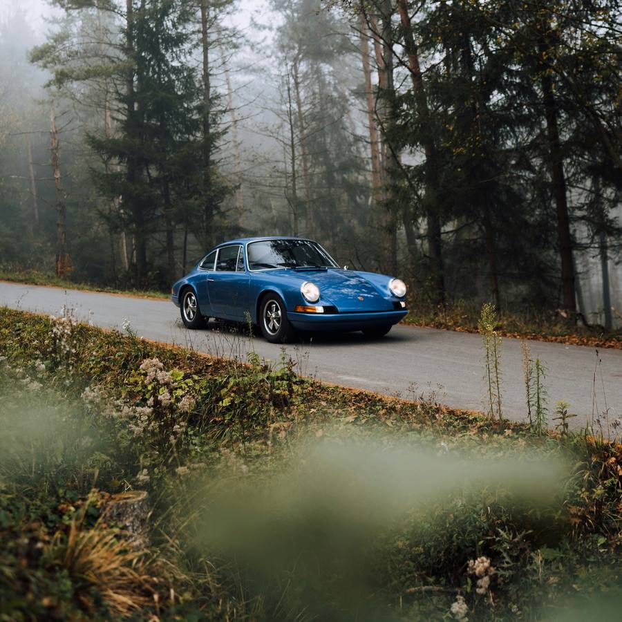 Porsche 911 clásico azul en una carretera de bosque