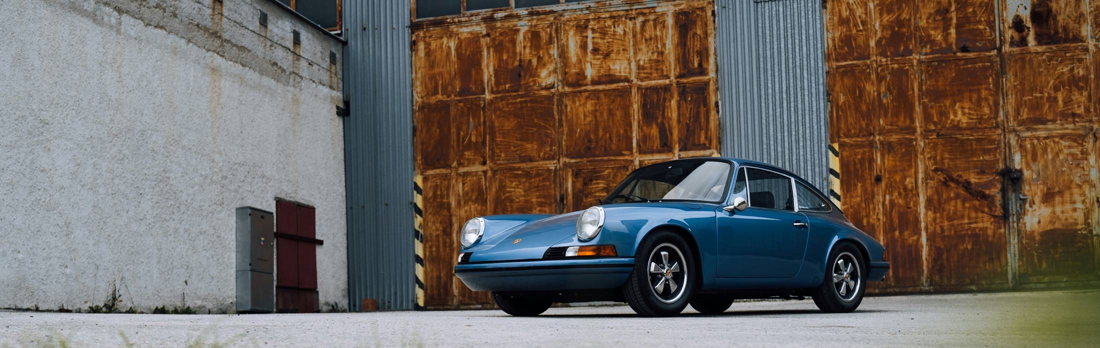 Porsche 911 clásico azul frente a puertas de hierro oxidado